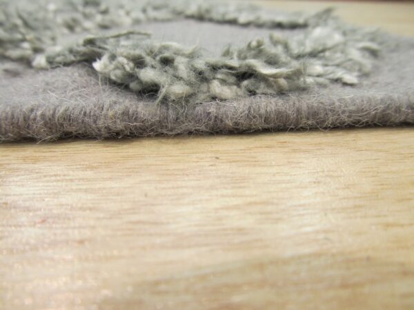 Low-angle view of a gray rug showing contrasting short and shaggy textures on wood.