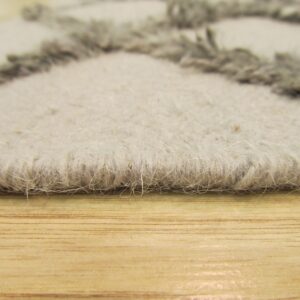 Textured gray and cream rug edge with shaggy accents rests on light brown wood flooring.