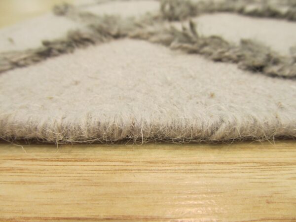 Textured gray and cream rug edge with shaggy accents rests on light brown wood flooring.