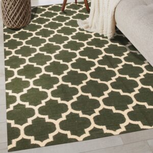 A low-pile dark green rug with a cream geometric trellis pattern lies on light flooring next to a couch.