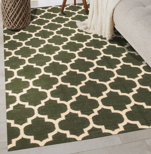 A low-pile dark green rug with a cream geometric trellis pattern lies on light flooring next to a couch.