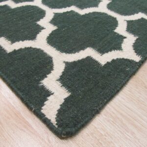 Textured green and cream geometric rug corner placed on light-toned, glossy plank flooring.