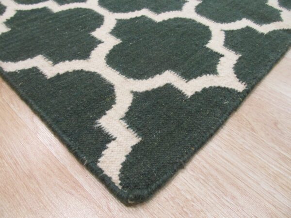 Textured green and cream geometric rug corner placed on light-toned, glossy plank flooring.