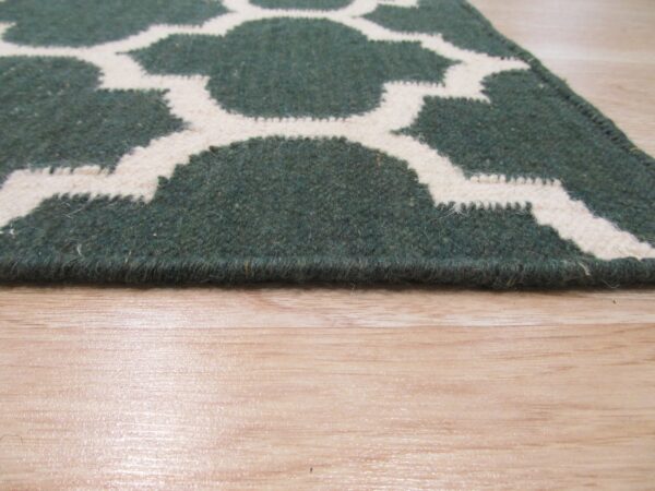Deep green and cream geometric rug with medium pile on glossy hardwood.