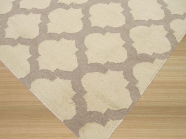 Corner view of a cream and taupe geometric rug on light-colored wooden planks.