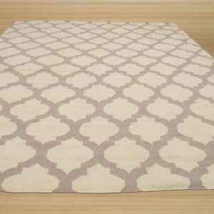 A rectangular rug with a cream and taupe geometric trellis pattern is displayed on light wooden flooring.