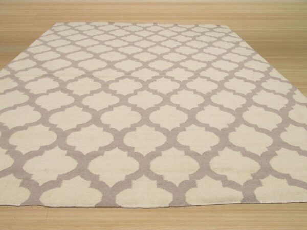 A rectangular rug with a cream and taupe geometric trellis pattern is displayed on light wooden flooring.