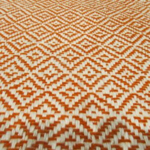 A flat woven textile featuring a repeating geometric diamond pattern in burnt orange and cream colors.