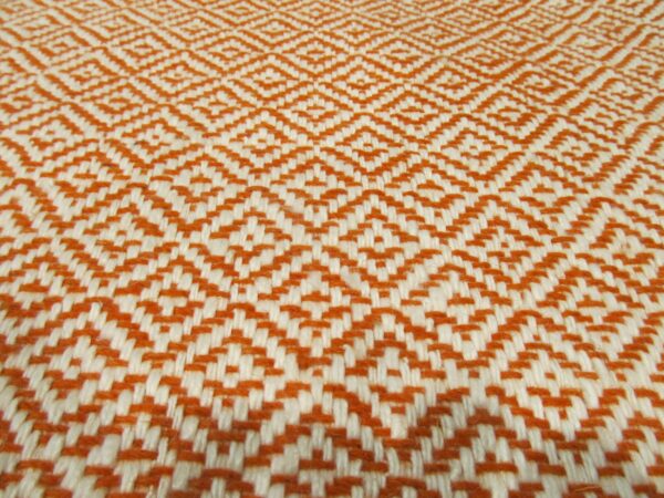 A flat woven textile featuring a repeating geometric diamond pattern in burnt orange and cream colors.