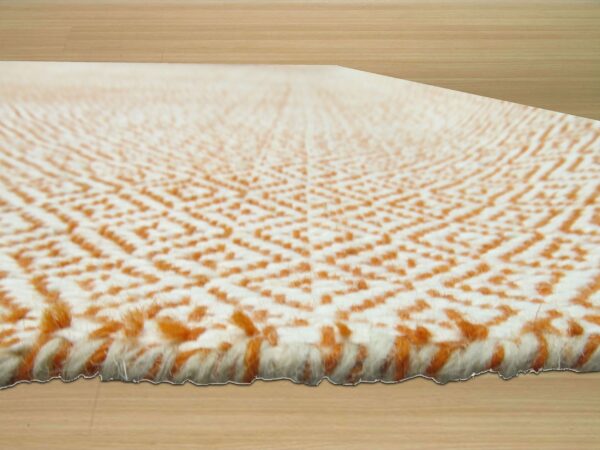 High-pile cream and terracotta rug with a textured geometric pattern rests on light wood planks.