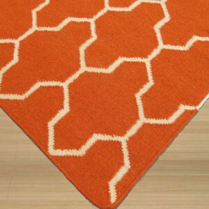 Orange low-pile rug displaying a cream interlocking geometric pattern on light blonde wood flooring.