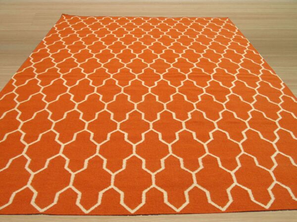 Orange low-pile rug with a repeating white geometric lattice pattern is displayed on light wood planks.