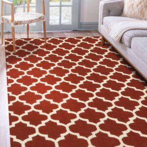 Rust and cream geometric trellis rug covers wood flooring near a light grey sofa and wooden chair.