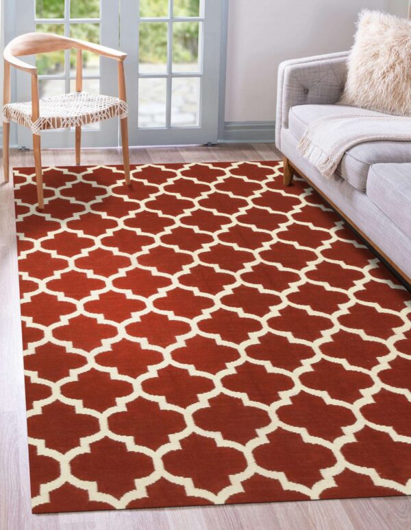 Rust and cream geometric trellis rug covers wood flooring near a light grey sofa and wooden chair.