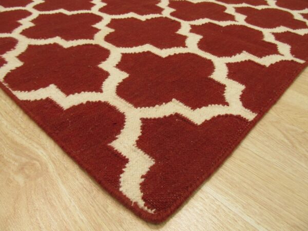 Terracotta and cream geometric rug featuring a trellis pattern resting on light wood flooring.
