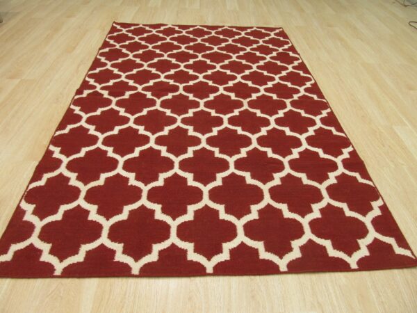 Low pile burgundy rug featuring a cream geometric quatrefoil pattern on light plank flooring.
