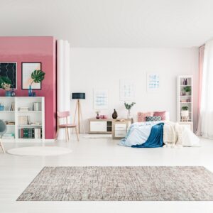 Distressed rectangular area rug in shades of pink, white, and brown on pale wood flooring.