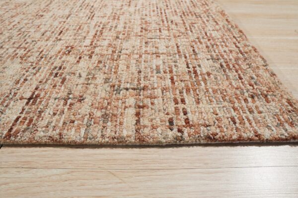 Textured loop pile rug in beige, rust, and brown colors lying on light wood flooring.