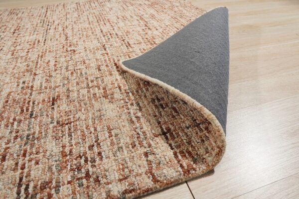 A rolled rug with textured beige and rust vertical stripes reveals a gray backing on light wood flooring.