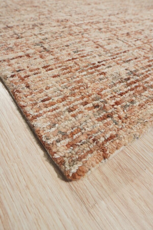 Chunky textured rug featuring mottled beige and rust horizontal stripes rests on light wooden flooring.