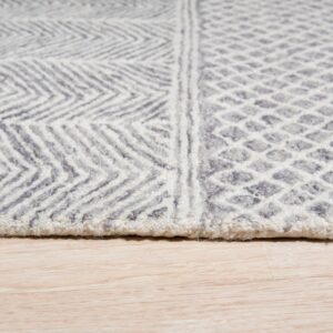 Close up of a gray and white textured rug with chevron and diamond patterns on light wood flooring.