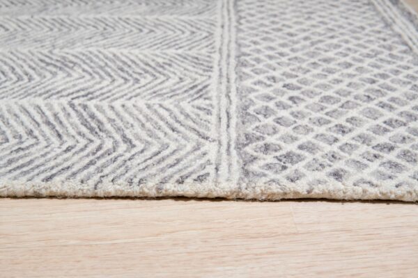 Close up of a gray and white textured rug with chevron and diamond patterns on light wood flooring.