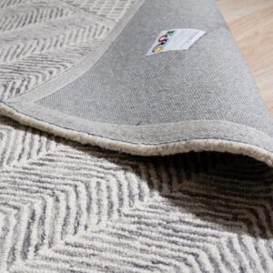 Textured gray and beige chevron rug rolled back, displaying its woven backing on light wood floors.