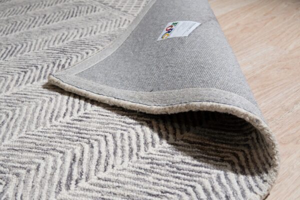 Textured gray and beige chevron rug rolled back, displaying its woven backing on light wood floors.
