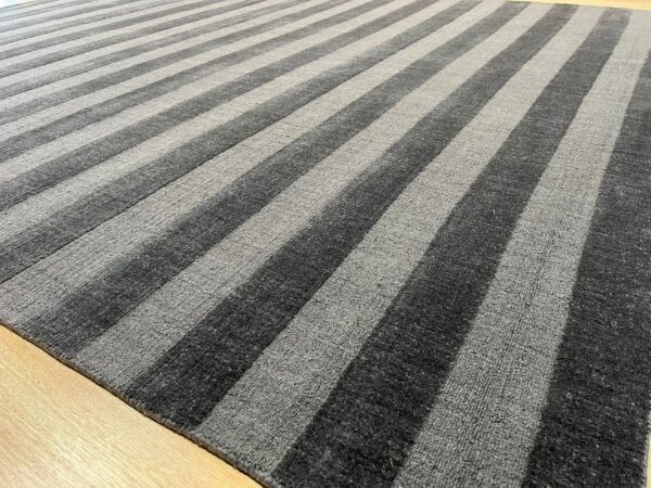 Textured rug with wide charcoal gray and light gray stripes resting on a blonde wood floor.