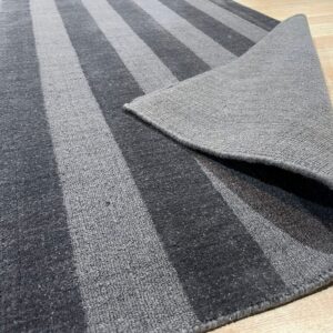 Gray striped rug featuring alternating pile textures, displayed partially folded on wood floor.