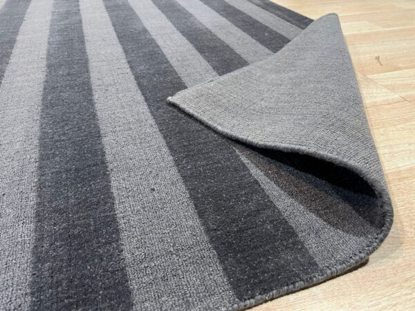 Gray striped rug featuring alternating pile textures, displayed partially folded on wood floor.