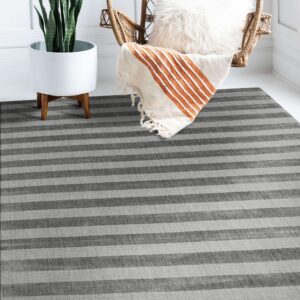 A striped grey rug on white wood flooring anchors a setting with a plant and wicker chair.