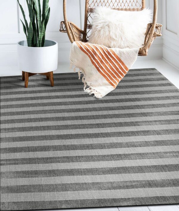 A striped grey rug on white wood flooring anchors a setting with a plant and wicker chair.