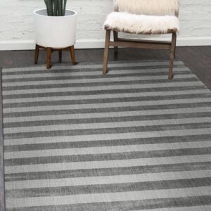 A striped gray rug lays on dark wood floor near a white brick wall, plant, and fur chair.
