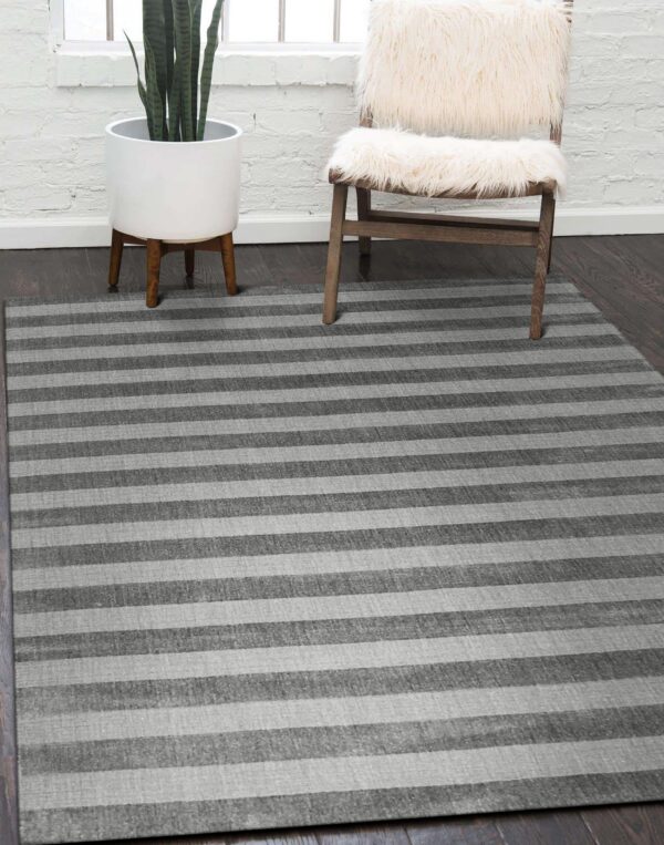 A striped gray rug lays on dark wood floor near a white brick wall, plant, and fur chair.