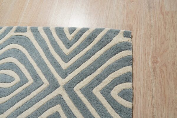 Blue and ivory high-pile rug with a carved geometric pattern rests on light wood planks.