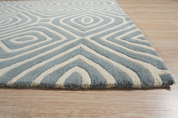 Textured blue and cream rug displays a geometric pattern of concentric diamonds on light wood flooring.