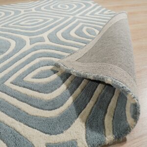 Textured blue and ivory rug with a geometric diamond pattern, partially rolled up on light wood flooring.