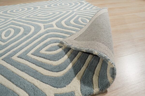 Textured blue and ivory rug with a geometric diamond pattern, partially rolled up on light wood flooring.