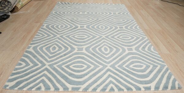 Blue and white rug with concentric diamond motifs and carved pile rests on light wood planks.