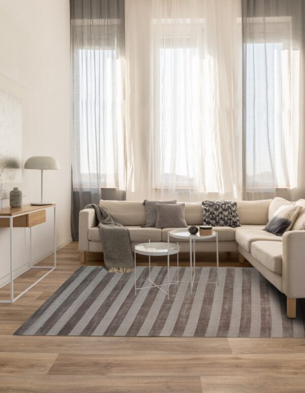 A gray and taupe striped area rug anchors a neutral living room with a cream sofa and wood floors.