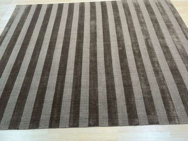 Rectangular rug featuring wide vertical stripes in dark brown and light gray on pale plank flooring.