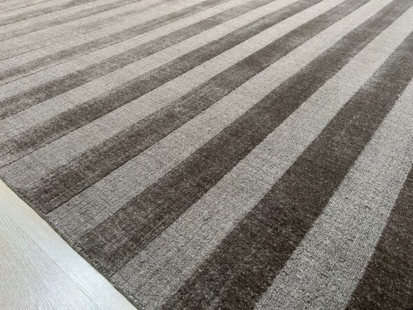 Textured striped rug featuring alternating bands of dark brown smooth pile and lighter gray loop pile on pale wood flooring.