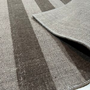 Gray and brown striped rug displayed on wood flooring, with one corner folded to show the backing.