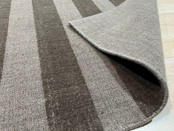 Gray and brown striped rug displayed on wood flooring, with one corner folded to show the backing.