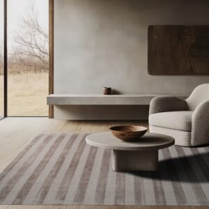 A low-pile striped gray rug covers light wood floors in a minimalist room with a round coffee table.