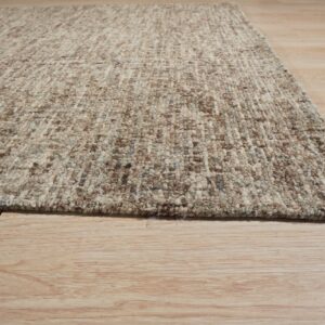 A close-up of the speckled, textured beige and brown rug edge on light wood flooring.