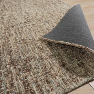 Close-up of a brown and beige looped rug, revealing the gray backing on light hardwood floor.