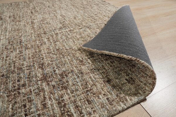 Close-up of a brown and beige looped rug, revealing the gray backing on light hardwood floor.
