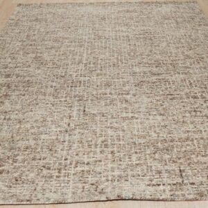 Chunky woven rug featuring an irregular beige and brown grid pattern displayed on light wood flooring.